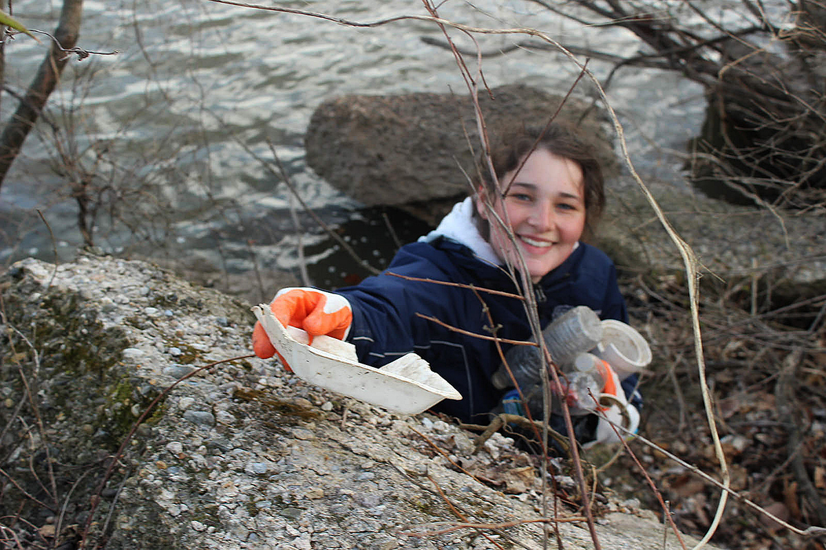 A volunteer from Parks and Recreation gathers trash from the banks of the Schuylkill River at Bartram's Garden. 